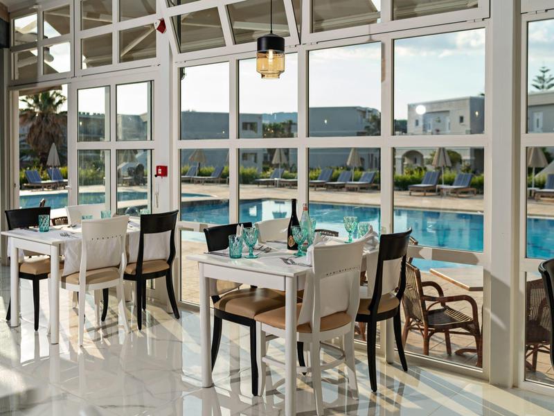 Hell verglaster Wintergarten mit Tischen und Stühlen neben einem blauen Swimmingpool draußen.