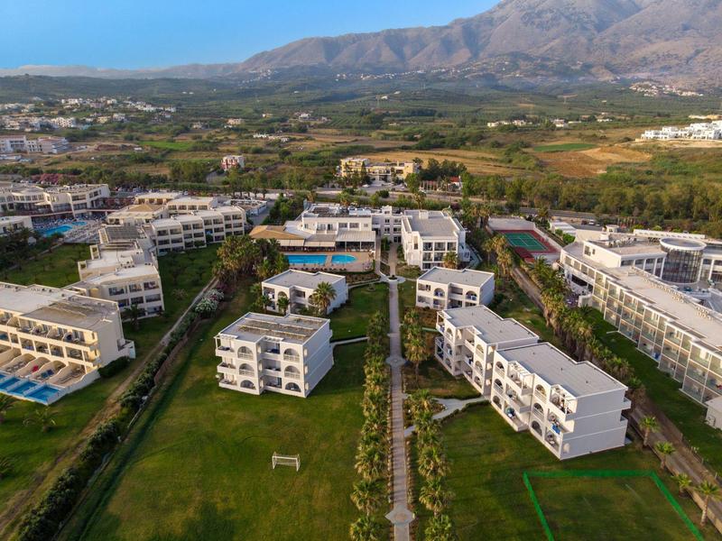 Großes Hotelresort mit mehreren weißen Gebäuden und Grünflächen vor bergiger Landschaft.