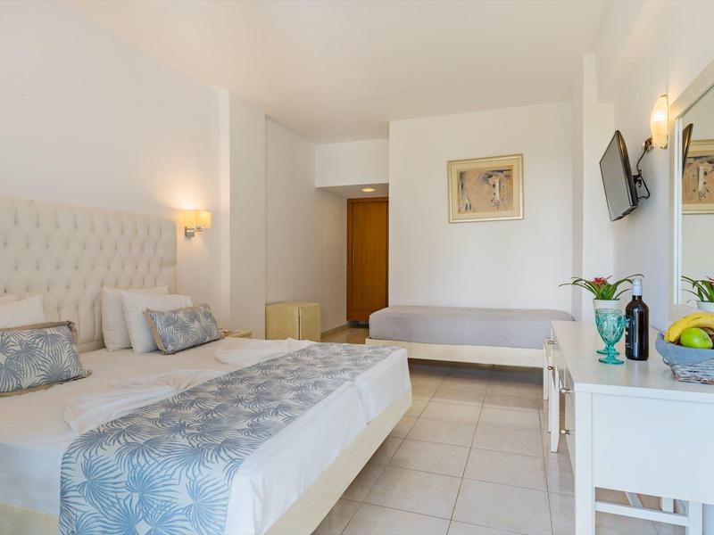 Hell eingerichtetes Hotelzimmer mit Doppelbett, Sofa, TV und Schreibtisch.