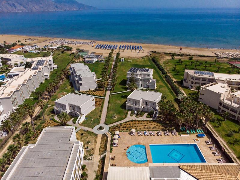 Luftaufnahme eines Resorts mit mehreren weißen Gebäuden, großem Pool, Liegestühlen und direktem Strandzugang.