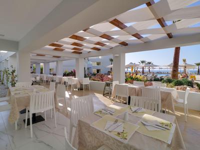 Střešní restaurace s bílými stoly a židlemi, dřevěnými střechovými akcenty a výhledem na moře.