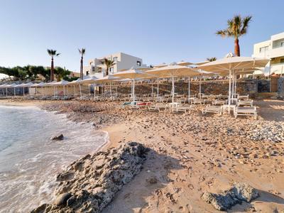 Piaszczysta plaża z parasolami i leżakami przed budynkiem hotelu o zachodzie słońca.