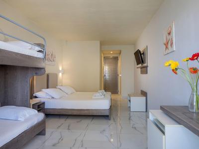 Jasny pokój hotelowy z łóżkiem piętrowym, łóżkiem podwójnym, telewizorem z płaskim ekranem i nowoczesnym umeblowaniem.