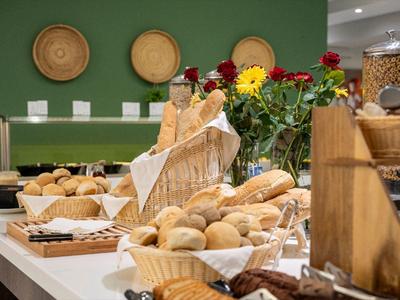 Różne rodzaje pieczywa i bułek w koszach na bufecie z zieloną ścianą i dekoracjami w tle.