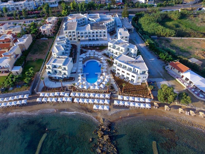 Widok z powietrza białego hotelu z basenem na plaży i leżakami wzdłuż wody.