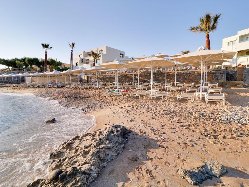 Piaszczysta plaża z parasolami i leżakami przed budynkiem hotelu o zachodzie słońca.