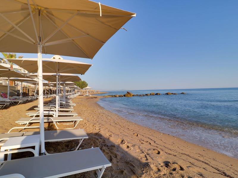 Pusta piaszczysta plaża z leżakami i parasolami przy spokojnym morzu pod błękitnym niebem.