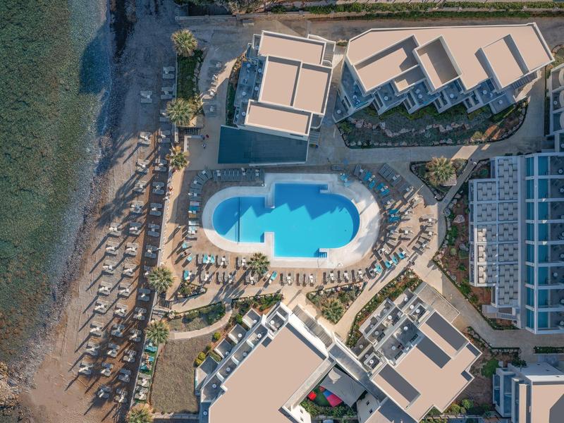 Widok z lotu ptaka na hotel z basenem, plażą i leżakami przy wodzie.