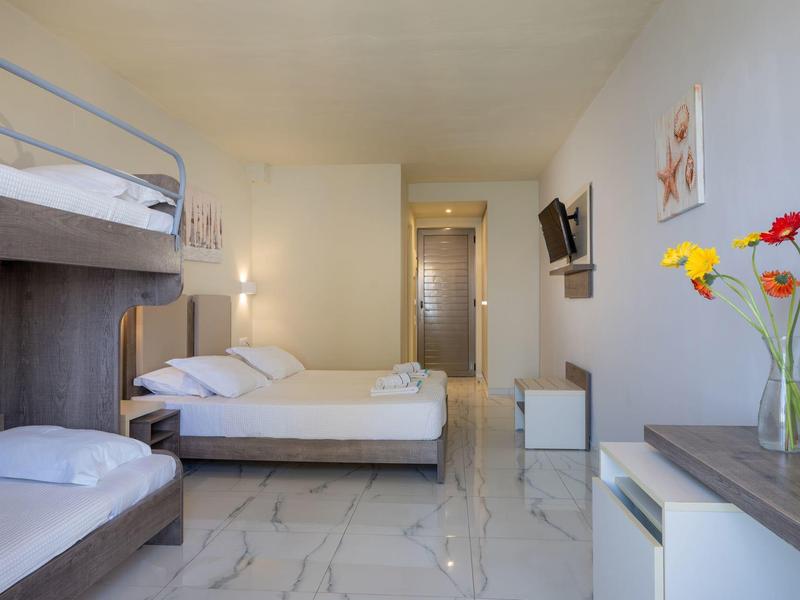 Jasny pokój hotelowy z łóżkiem piętrowym, łóżkiem podwójnym, telewizorem z płaskim ekranem i nowoczesnym umeblowaniem.