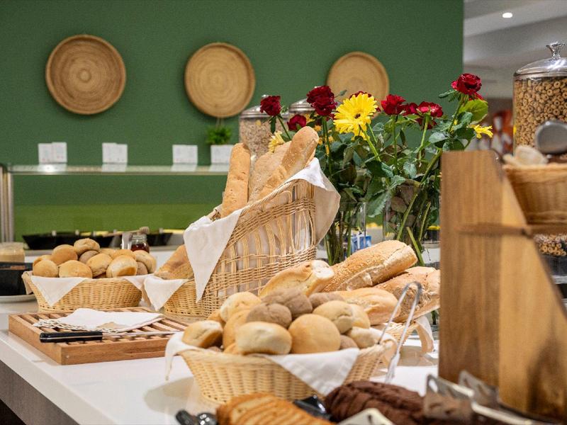 Różne rodzaje pieczywa i bułek w koszach na bufecie z zieloną ścianą i dekoracjami w tle.