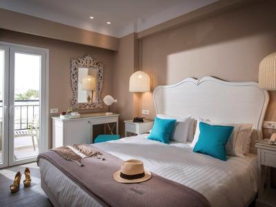 Elegant hotel room with double bed, white furniture, and balcony with outdoor view.