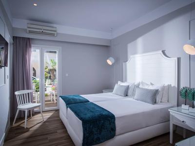 Modernes Hotelzimmer mit zwei Betten, blauem Tagesdecke und Zugang zu einem Balkon.