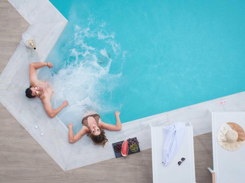 Two women relaxing in the pool with a book and drinks nearby on the terrace.