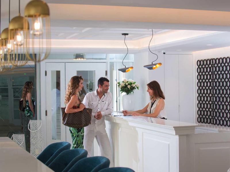 Hotel reception with guests and staff in a modern, bright setting.