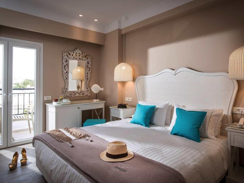 Elegant hotel room with double bed, white furniture, and balcony with outdoor view.