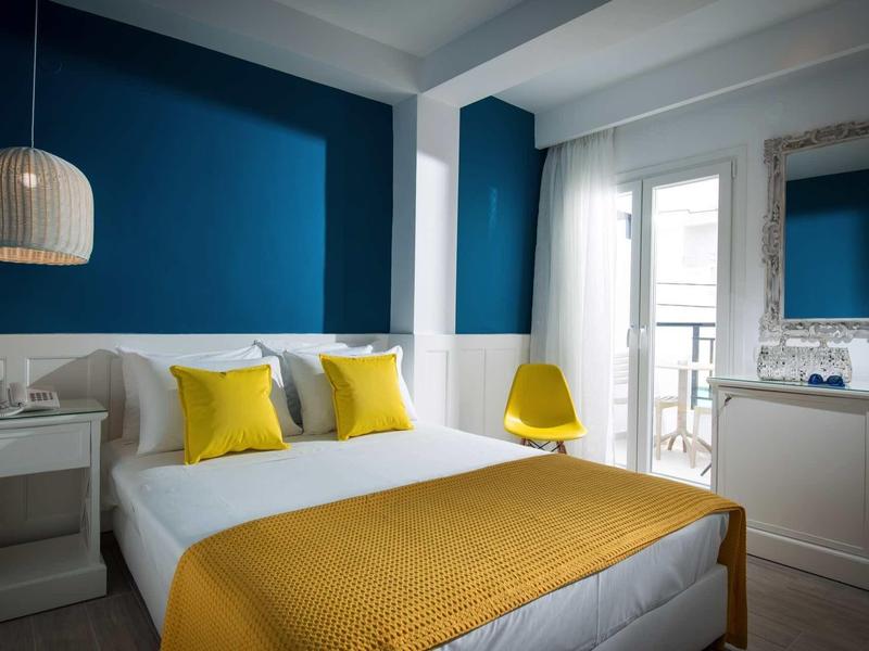 Modern hotel room with double bed, yellow accents, and balcony with glass doors.