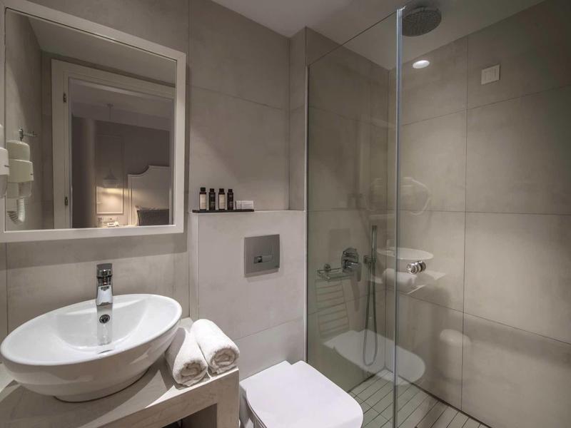 Modern bathroom with round sink, glass shower enclosure, and gray tiles.