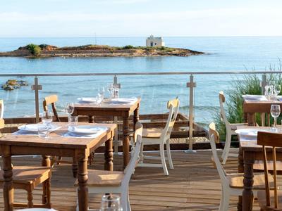 Venkovní restaurace s dřevěnými stoly a výhledem na moře a malý ostrov.