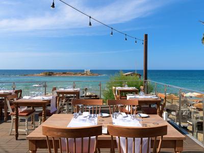 Venkovní restaurace s dřevěnými stoly s výhledem na moře pod jasnou oblohou.