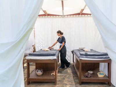 Osoba připravuje dvě masážní lehátka v otevřeném bílém stanu.