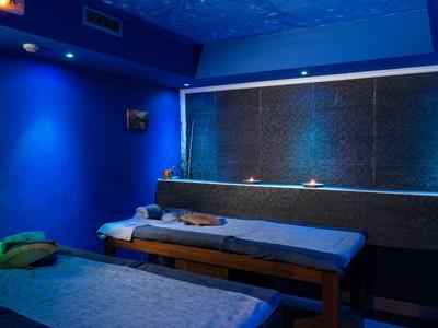 Tmavá wellness místnost s modrým osvětlením a dvěma masážními lehátky, minimalistická výzdoba.