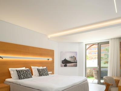 Moderní hotelový pokoj s manželskou postelí, dřevěnou stěnou a přístupem na balkon.