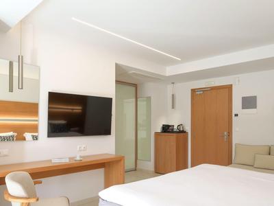 Světý hotelový pokoj s velkou postelí, televizí na stěně, psacím stolem a moderním vybavením.