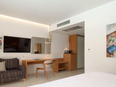 Moderně zařízený hotelový pokoj s TV, pracovním stolem a posezením.