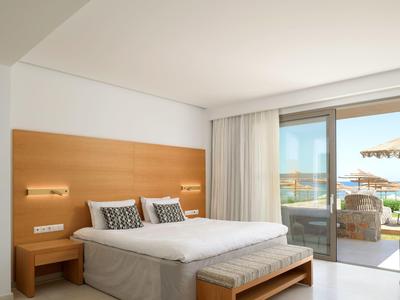 Světly hotelový pokoj s manželskou postelí a terasou s výhledem na moře.