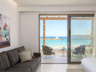 Světly hotelový pokoj s pohovkou, postelí a balkonem s výhledem na moře.