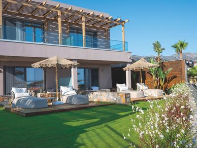 Balcón moderno de hotel con tumbonas, sombrillas y vista a un jardín bien cuidado.