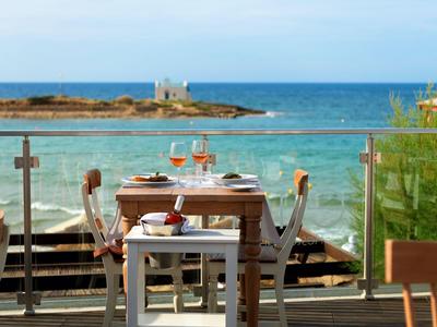 Una mesa puesta con dos copas de vino en una terraza con vista al mar.