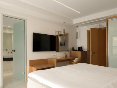 Svět hotelový pokoj s manželskou postelí, psacím stolem, televizí na stěně a viditelnou koupelnou.