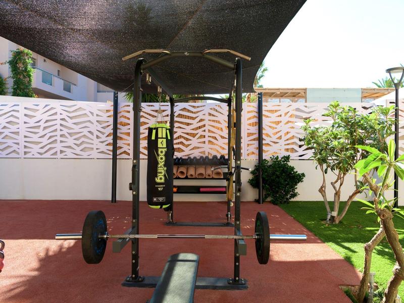 Venkovní fitness prostor s hrazdou na shyby a činkou na červené podlaze vedle zahrady