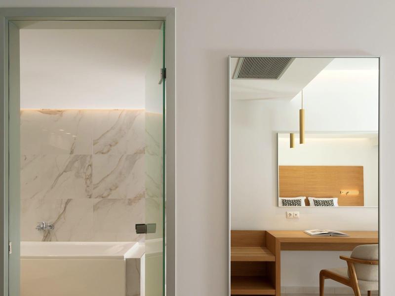 Moderní hotelová koupelna s mramorovou stěnou a přilehlým pokojem se zrcadlem a dřevěnými detaily