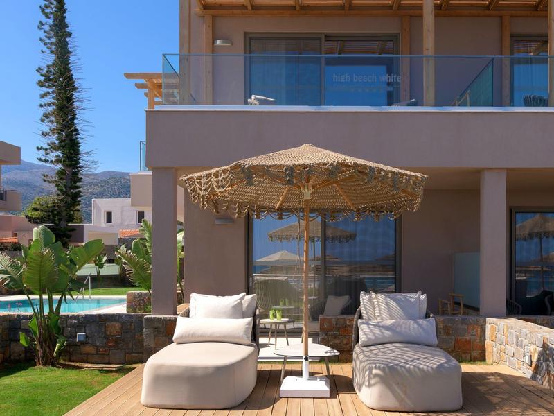 Dva pohodlná lehátka s polštáři a slunečníkem na terase před moderním domem.