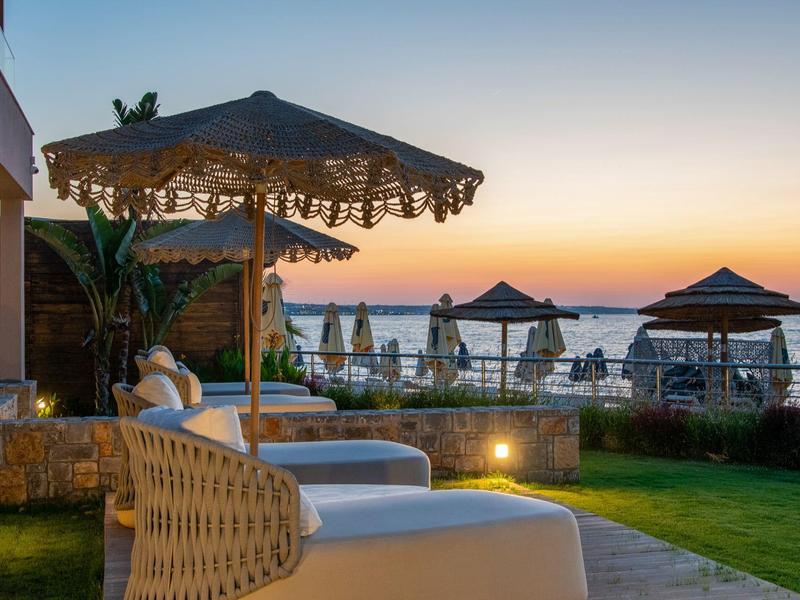 Pohodlná lehátka s parasoly v zahradě s výhledem na moře za západu slunce.