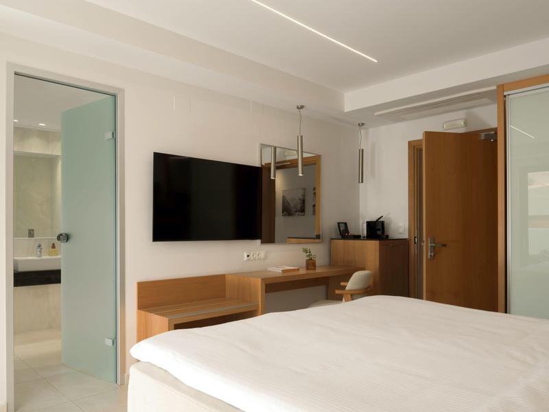 Svět hotelový pokoj s manželskou postelí, psacím stolem, televizí na stěně a viditelnou koupelnou.