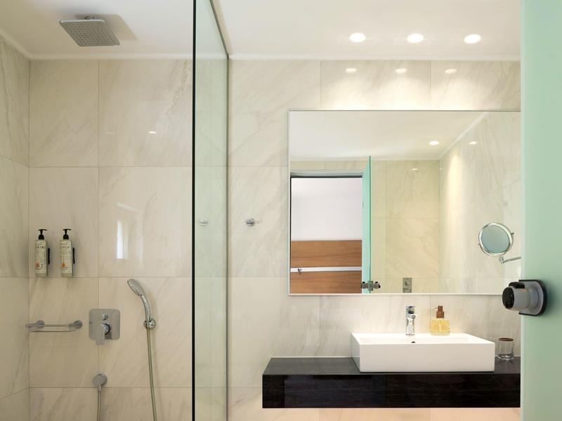 Moderní hotelová koupelna se skleněným sprchovým koutem, umyvadlem a zrcadlovou stěnou.