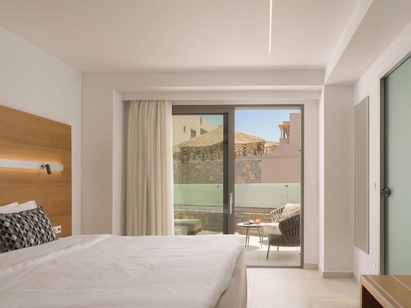 Světý hotelový pokoj s velkou postelí, malým balkonem a moderním nábytkem.