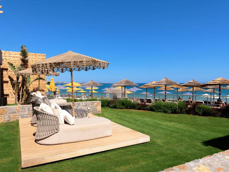 Lehátka a slunečníky u bazénu s výhledem na moře za slunečného dne.