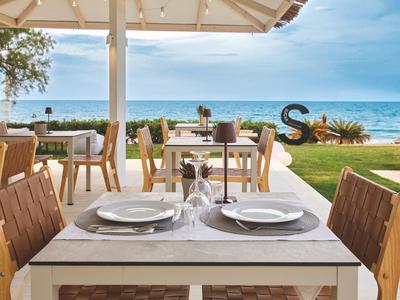 Terrasse mit Holztischen, Stühlen und gedecktem Tisch mit Meerblick im Hintergrund.