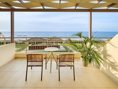 Terrasse mit Tisch, zwei Stühlen und Blick auf das Meer bei klarem Himmel.