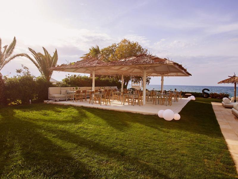 Open pavilion with thatched roof beside well-maintained lawn and palm trees at sunset