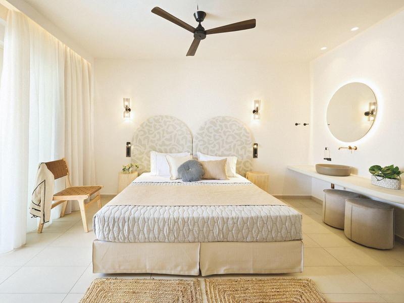 Bright hotel room with king-size bed, ceiling fan, and modern vanity with round mirror.