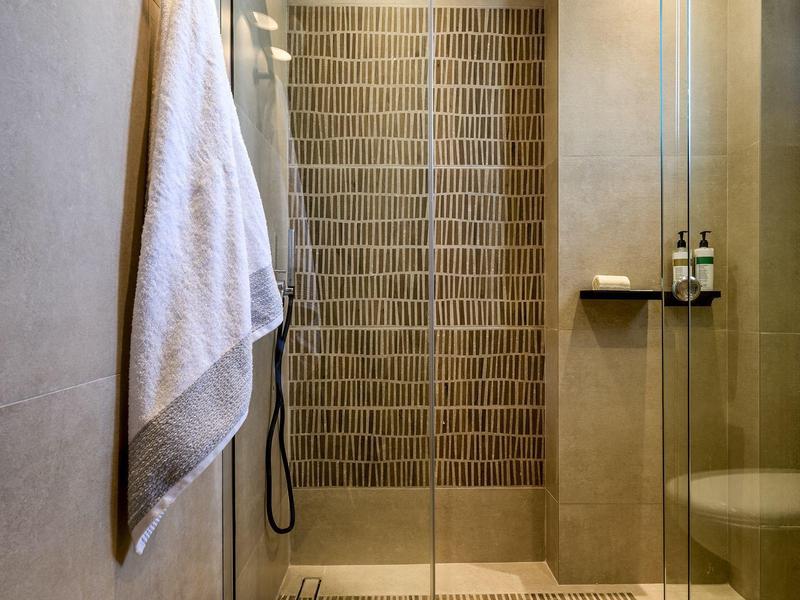 Modern shower with glass door, towel on wall, and brown tiles in hotel bathroom.