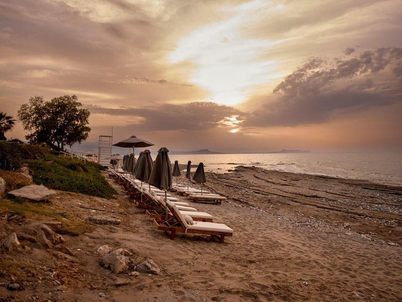 Empty beach with lounge chairs at sunset under a cloudy sky.