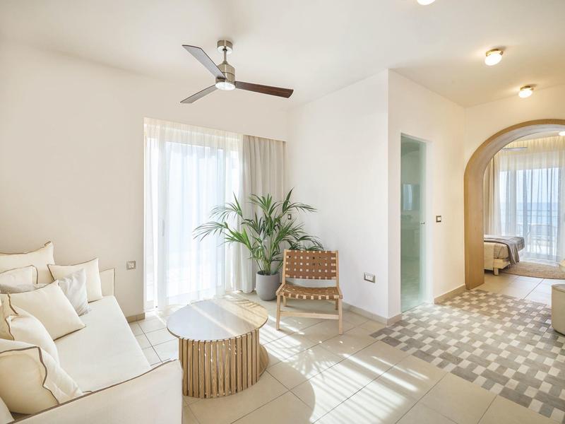 Bright living area with sofa, plants, modern fan, and passage to bedroom.