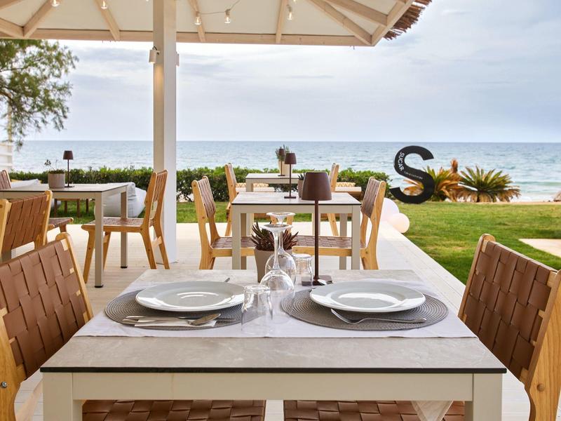 A table with two chairs on a terrace overlooking the sea under a clear sky.
