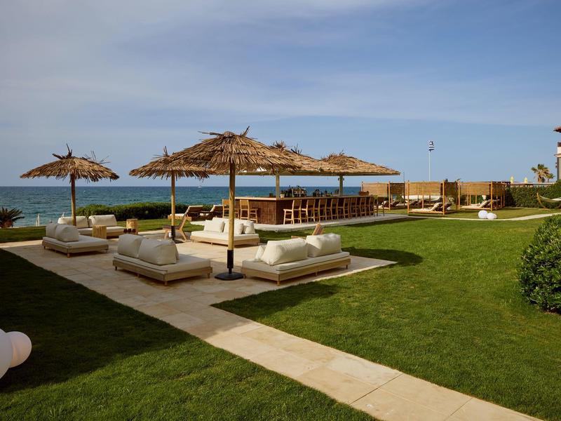 Luxury pool area with sun umbrellas and loungers next to the sea under clear sky.